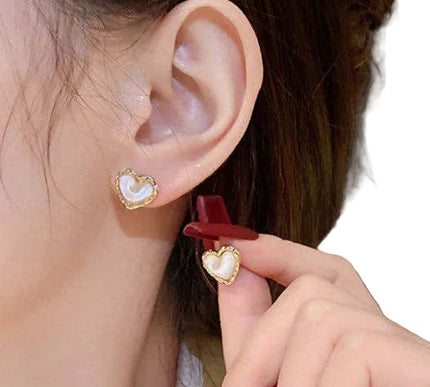 Close-up of an ear with a gold earring, hand holding a red hair clip, and blurred background.