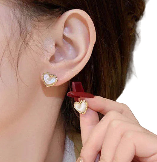 Close-up of an ear with a gold earring, hand holding a red hair clip, and blurred background.