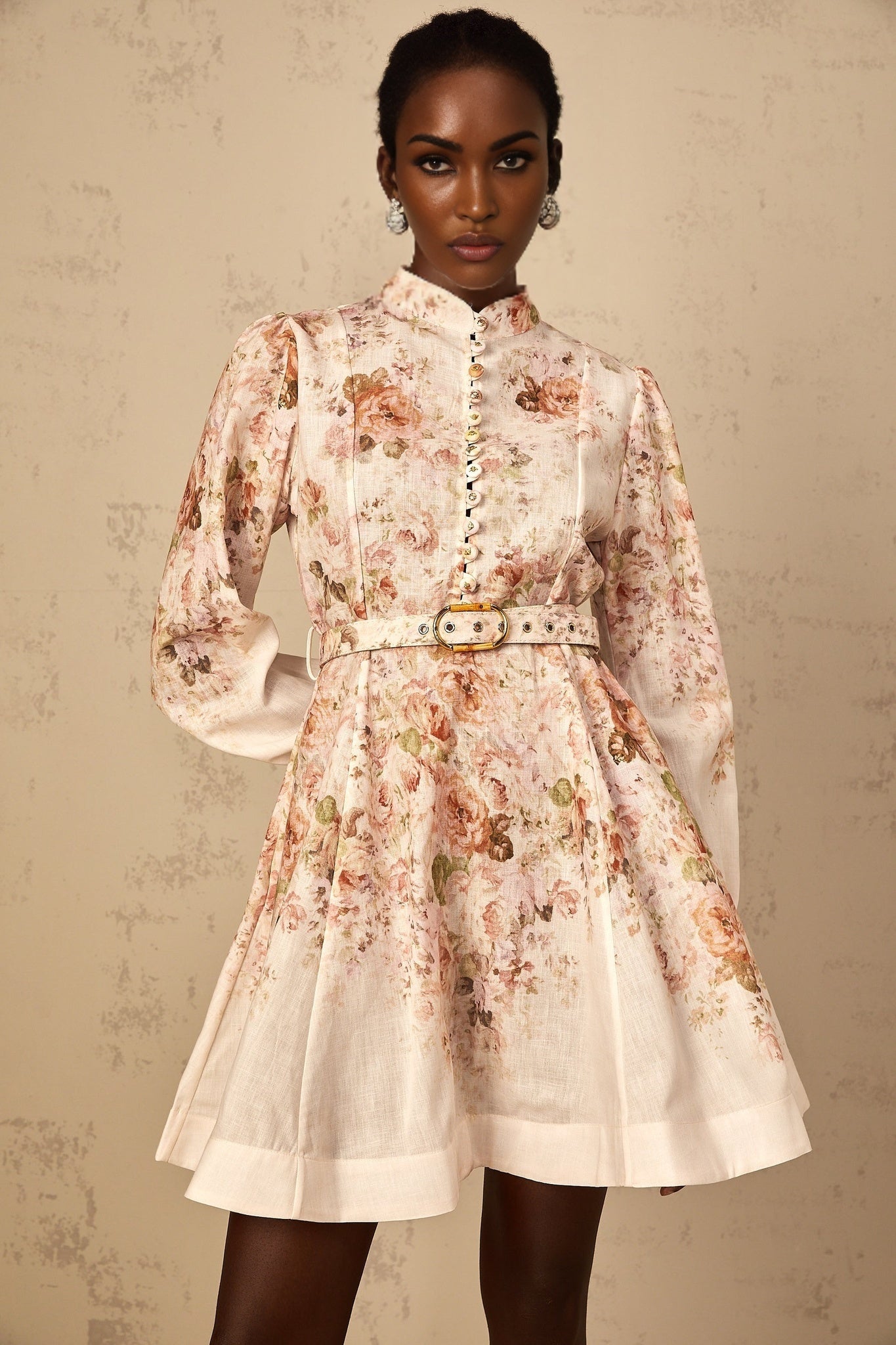 A beige mini dress with a floral print pattern worn by a female model standing against a plain background