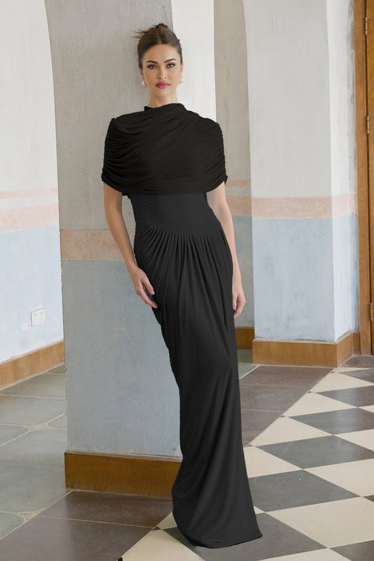 A black asymmetric maxi dress with pleated detailing worn by a model standing against a plain background