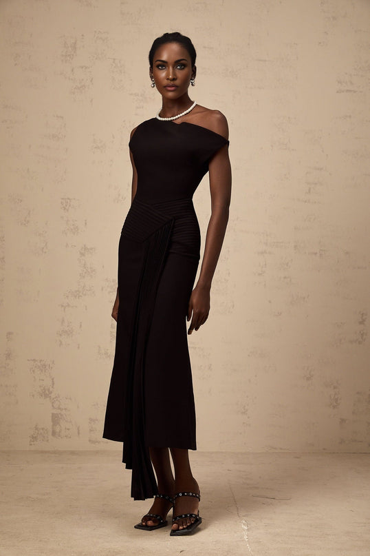 A black asymmetric midi dress with draped fabric details worn by a model standing against a plain background