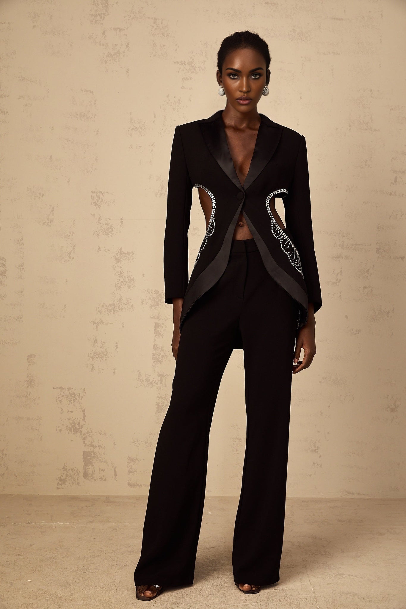 A black blazer and trouser set featuring cutout details and embellishments The blazer has a tailored fit with decorative elements while the trousers are sleek and coordinating Elegant formal attire for women