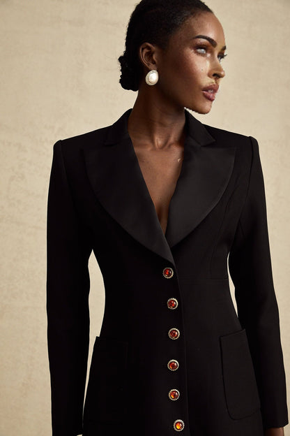 A black blazer dress with a singlebreasted design worn by a model standing against a plain background