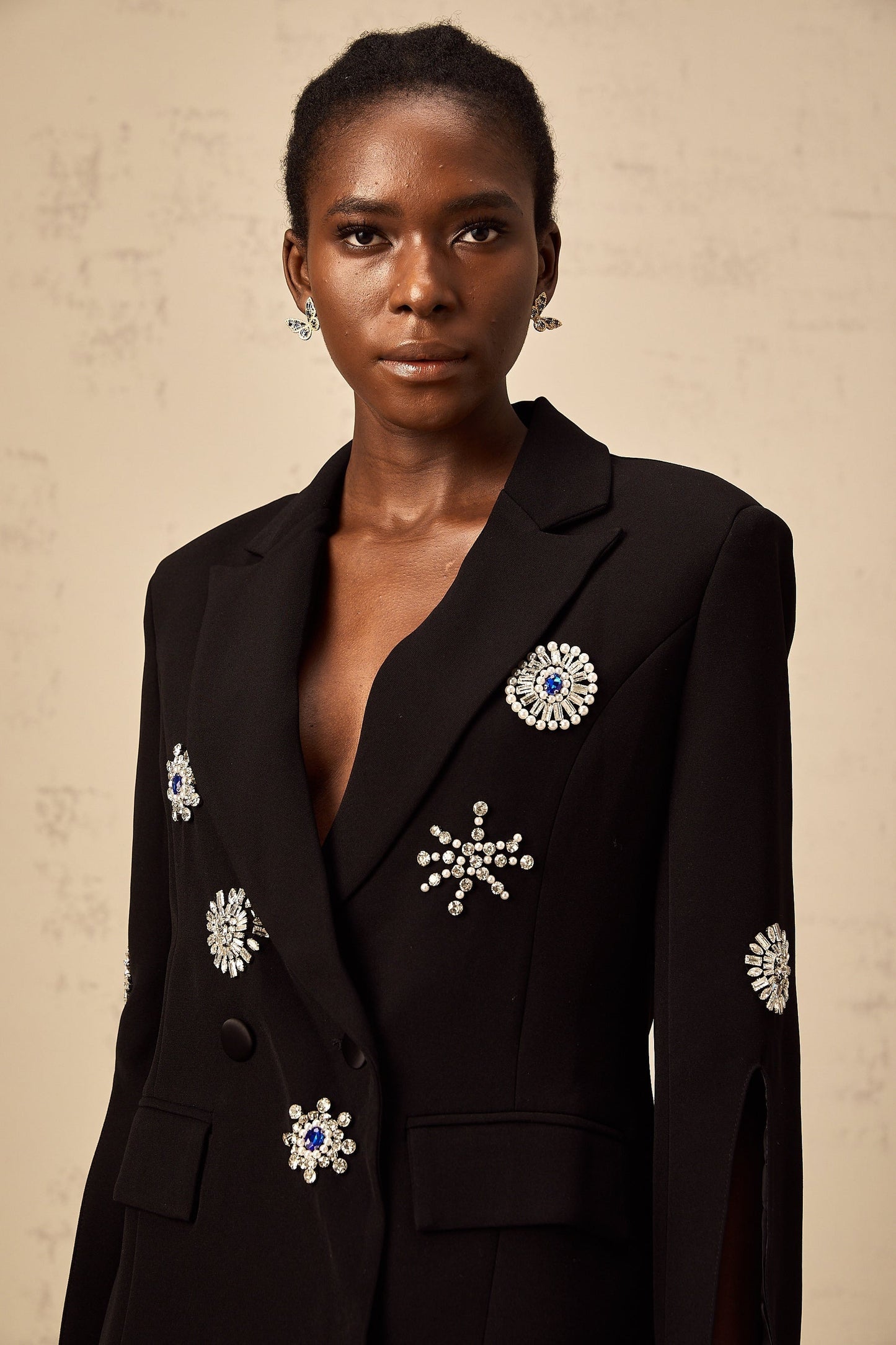A black blazer with crystal embellishments along the cuffs featuring slits The jacket has a tailored fit and sleek design suitable for formal or evening wear