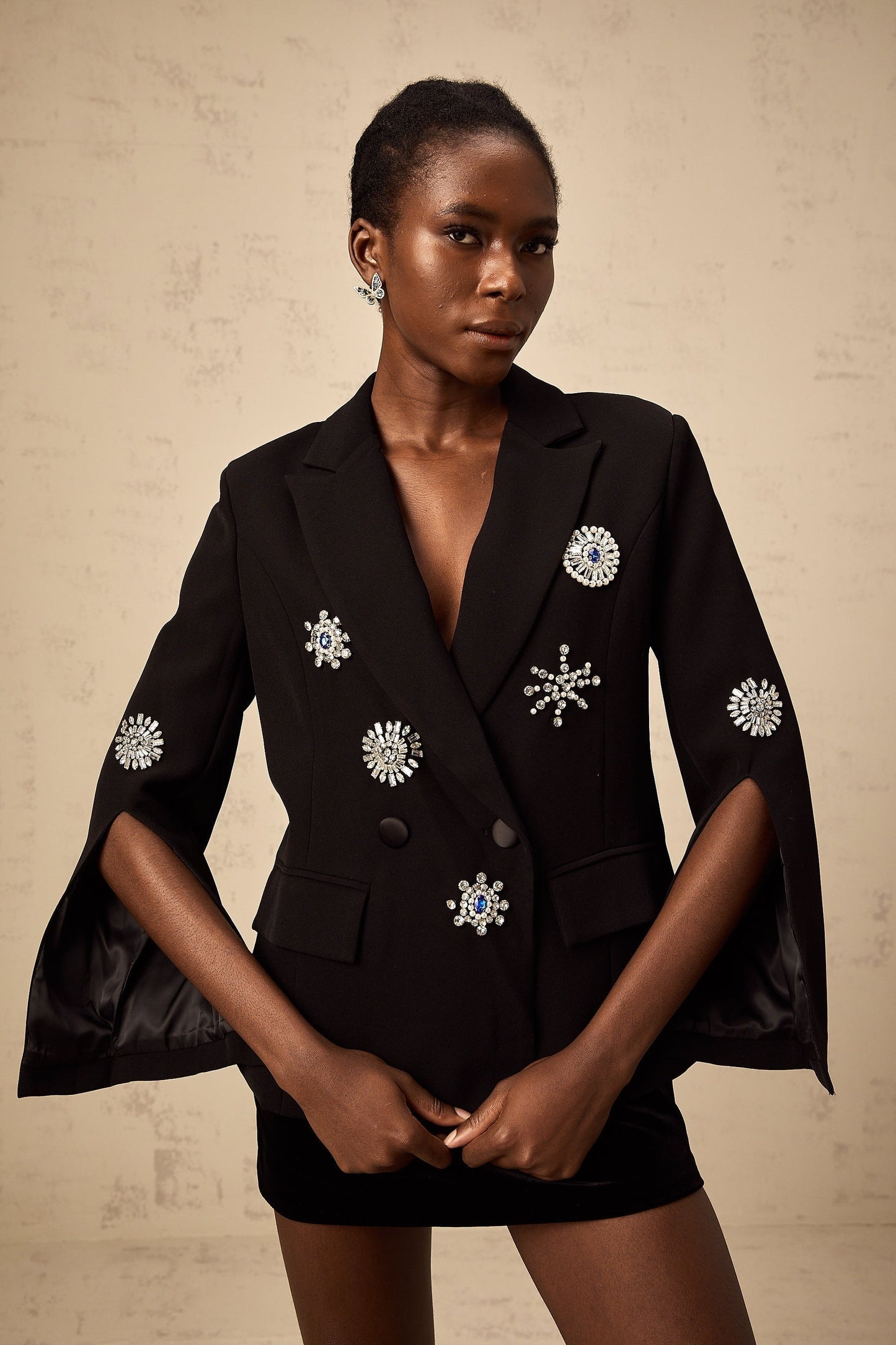 A black blazer with crystal embellishments on the cuffs featuring slits The blazer has a sleek design and appears to be made of a luxurious fabric The crystals add a touch of glamour to the formal attire