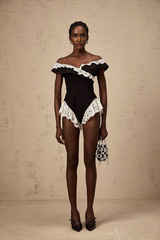 A black bodysuit with delicate lace trim along the edges worn by a female model against a plain background