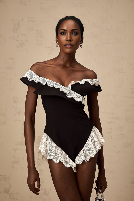 A black bodysuit with delicate lace trim worn by a model standing against a plain background