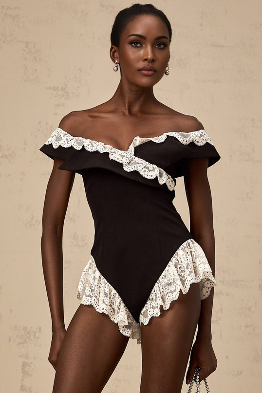 A black bodysuit with lace trim detailing worn by a female model standing against a plain background