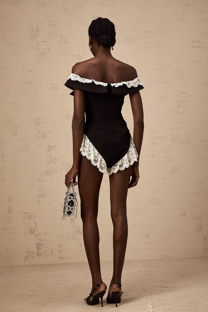 A black bodysuit with lace trim detailing worn by a model standing against a plain background