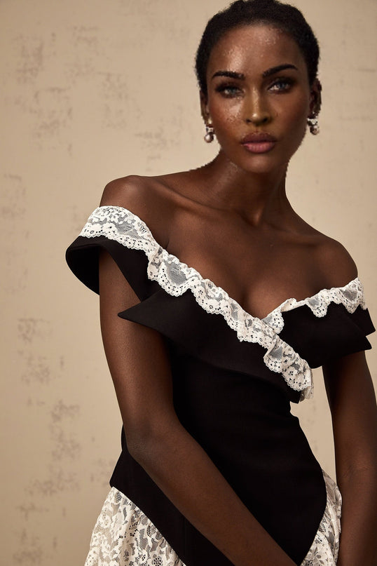 A black bodysuit with lace trim details worn by a model against a plain background
