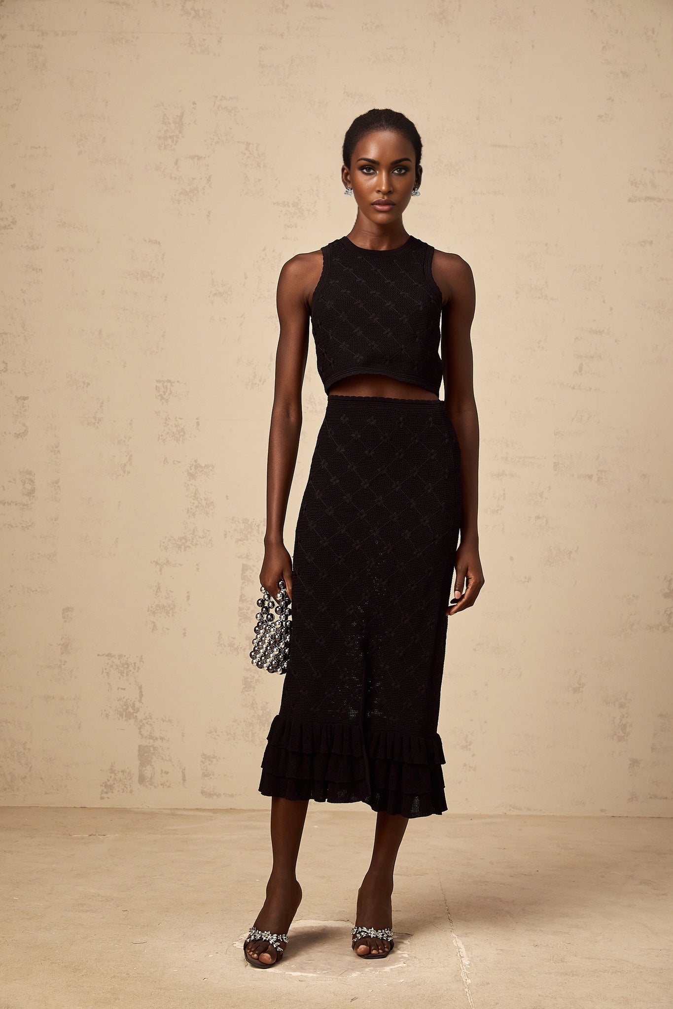 A black crochet knit matching set consisting of a top and skirt The top is sleeveless with a scoop neckline and the skirt is knee length Both pieces feature an intricate crochet pattern throughout