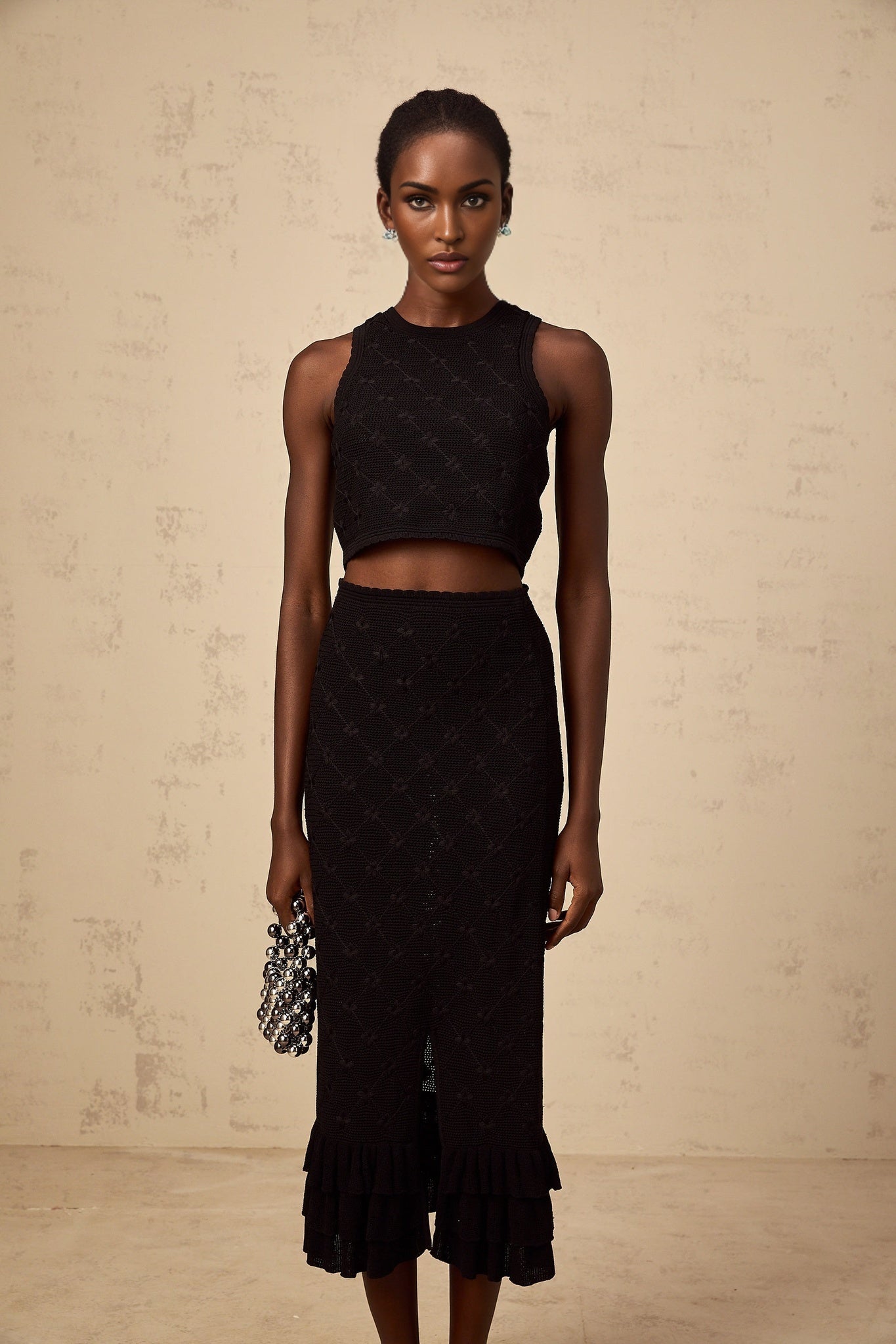 A black crochet knit matching set consisting of a top and skirt worn by a model against a plain background