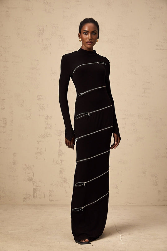 A black fitted maxi dress with zipper details worn by a model standing against a plain background