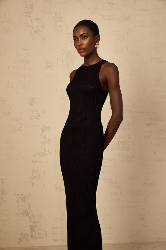 A black fitted ribbed knit maxi dress on a model standing against a plain background