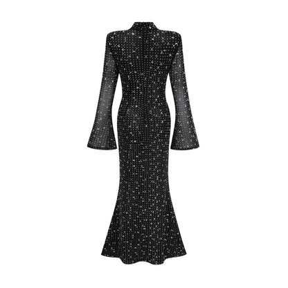 A black floor length maxi dress with sheer elements and embellished details worn by a model standing against a plain background