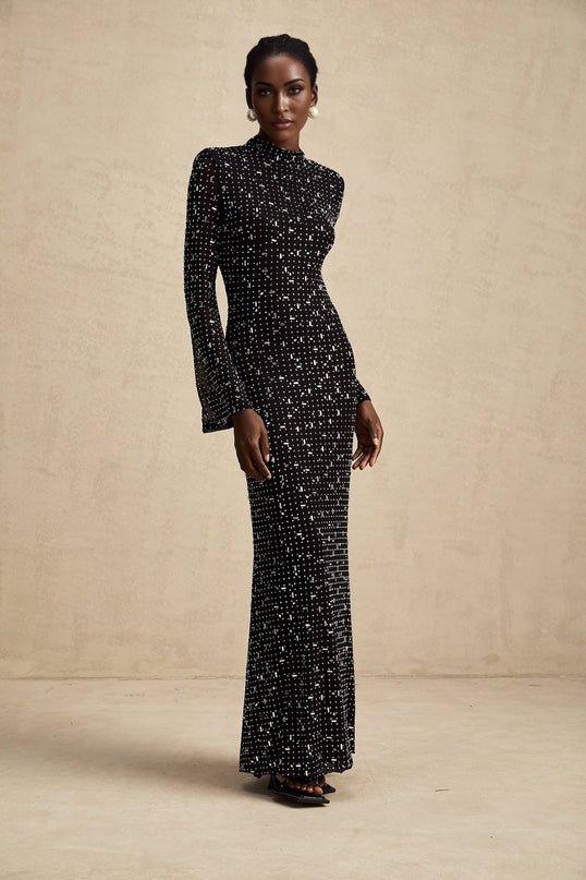 A black floor length maxi dress with sheer elements and embellished details worn by a model