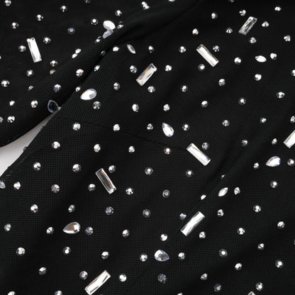 A black floor length maxi dress with sheer panels and embellished details worn by a model against a plain background