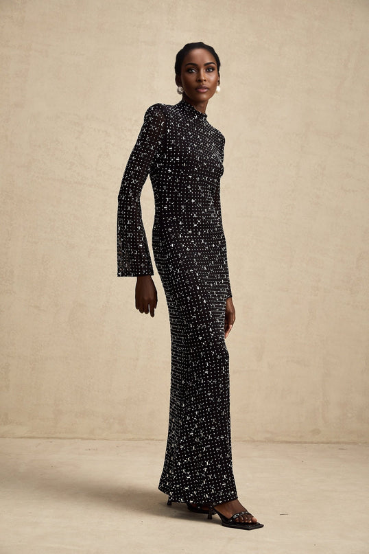 A black floor length maxi dress with sheer panels and embellished details worn by a model