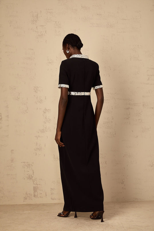 A black floorlength maxi dress with a front slit and crystal embellishments worn by a model standing against a plain background