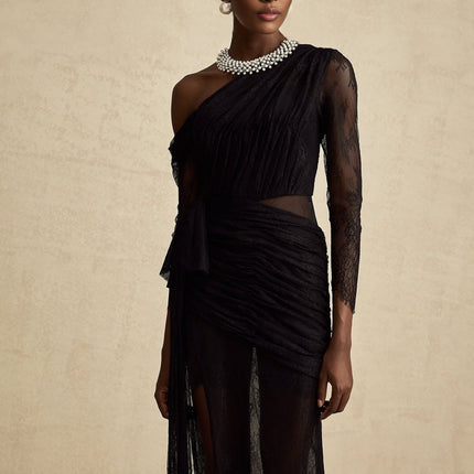 A black floorlength maxi dress with a single shoulder strap and a cut out detail on one side worn by a model against a plain background