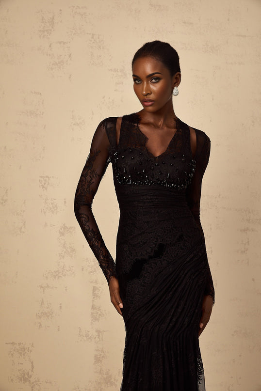 A black floorlength mermaid style dress with floral lace pattern worn by a model standing in a neutral background