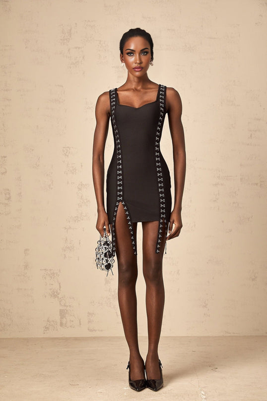 A black formfitting mini dress with hookandeye closures worn by a model standing against a plain background