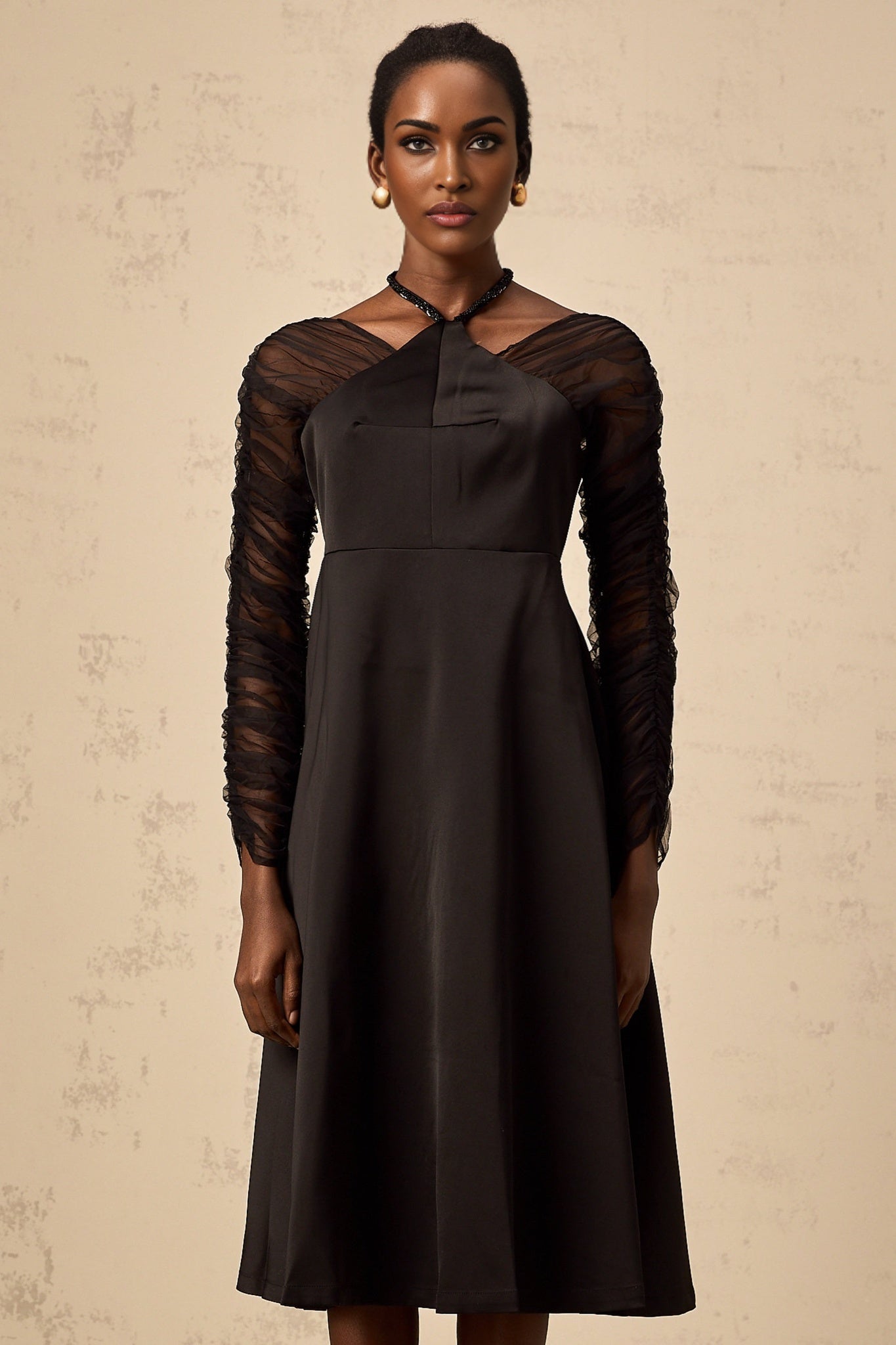 A black halterneck midi dress with panel detailing worn by a model against a plain background