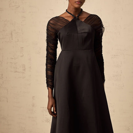 A black halterneck midi dress with panel detailing worn by a model standing against a plain background