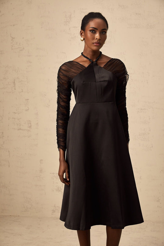 A black halterneck midi dress with panel detailing worn by a model standing against a plain background