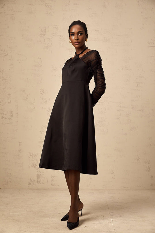 A black halterneck midi dress with panel detailing worn by a model standing against a plain background