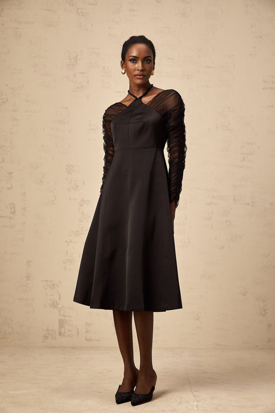 A black halterneck midi dress with panelled design worn by a model standing against a plain background