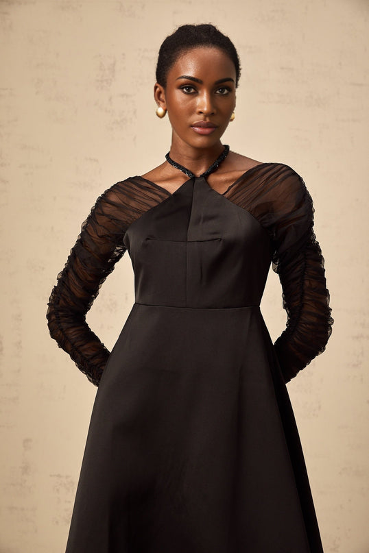 A black halterneck midi dress with panelled design worn by a model standing against a plain background