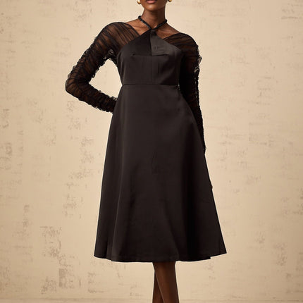 A black halterneck midi dress with panelled design worn by a model standing against a plain background