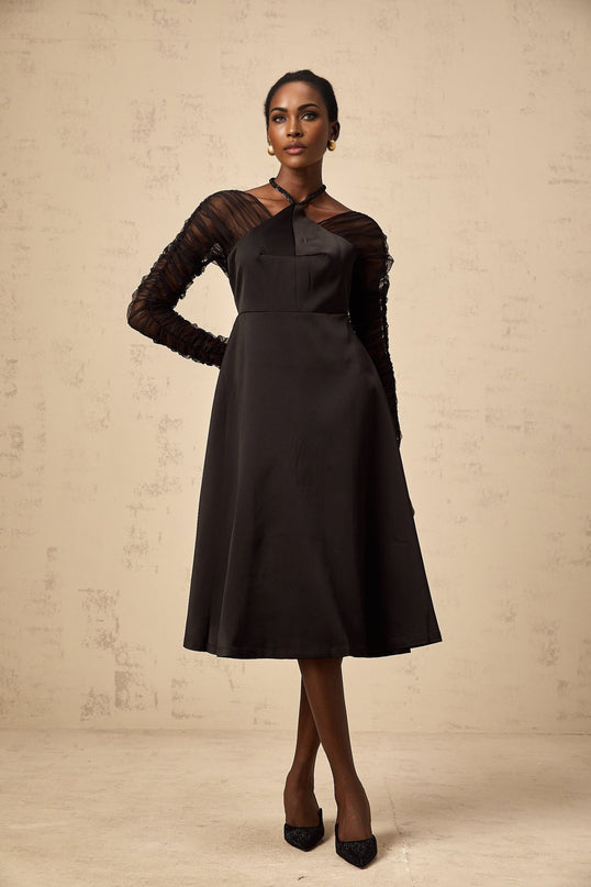 A black halterneck midi dress with panelled design worn by a model standing against a plain background