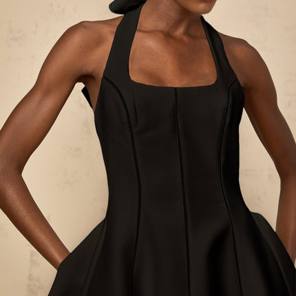 A black halterneck mini dress with a bow detail featuring a fitted silhouette and a short hemline