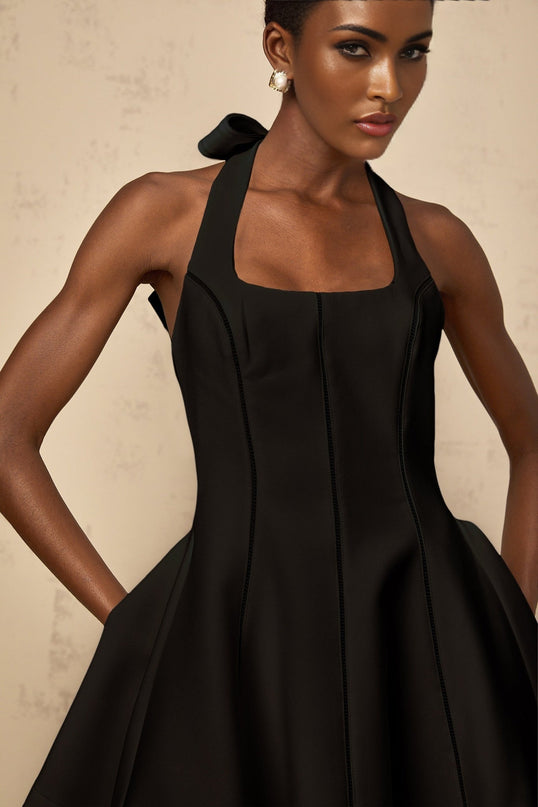 A black halterneck mini dress with a bow detail featuring a fitted silhouette and a short hemline