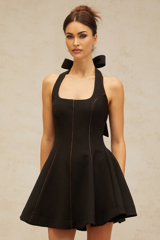 A black halterneck mini dress with a bow detail worn by a model standing against a plain background