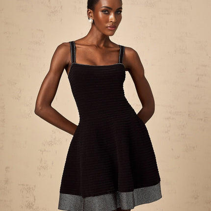 A black knit mini dress with flared skirt and studded details worn by a model against a plain background
