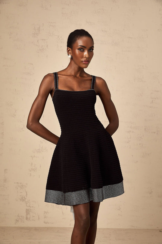 A black knit mini dress with flared skirt and studded details worn by a model against a plain background