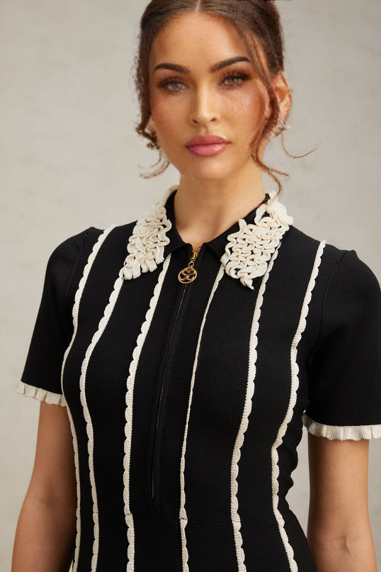 A black knit mini dress with vertical white stripes and ruffle trim details on a female model