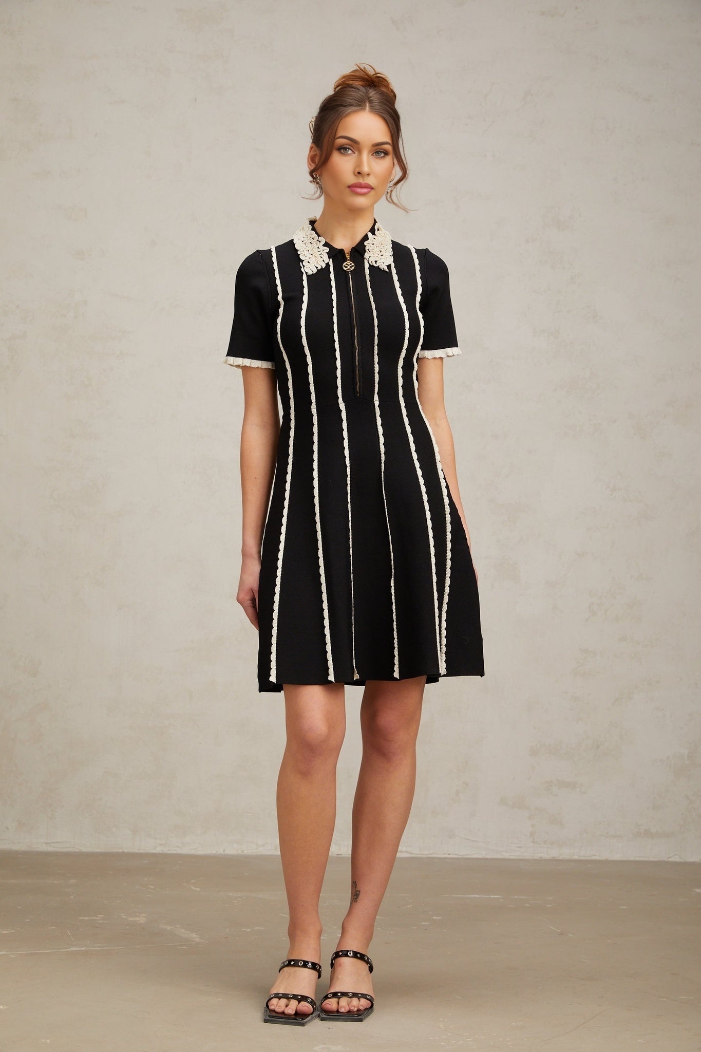 A black knit mini dress with vertical white stripes and ruffle trim details on a female model