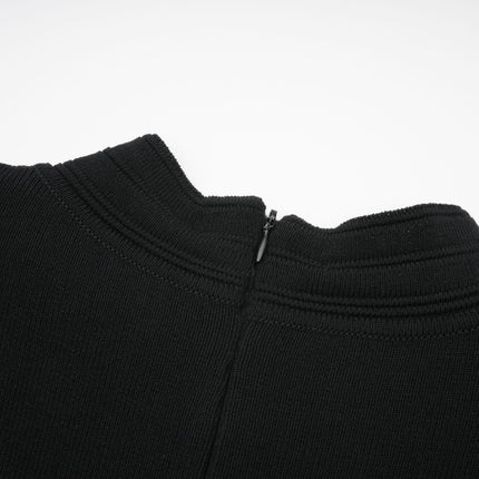 A black knitted mini dress with ruffled details and embellishments worn by a model standing against a plain background