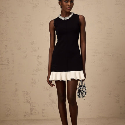 A black knitted mini dress with ruffled details and faux pearl embellishments displayed on a mannequin or model