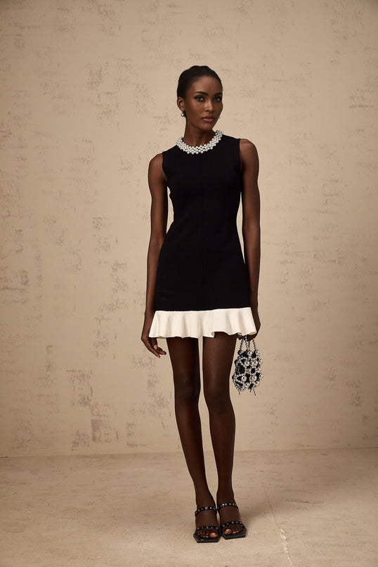 A black knitted mini dress with ruffled details and faux pearl embellishments displayed on a mannequin or model