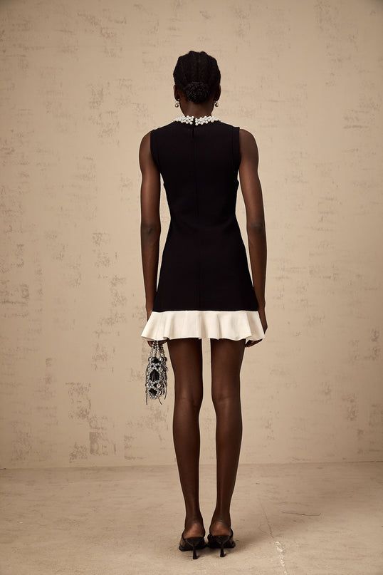 A black knitted mini dress with ruffled details and faux pearl embellishments featuring a short hemline and fitted silhouette
