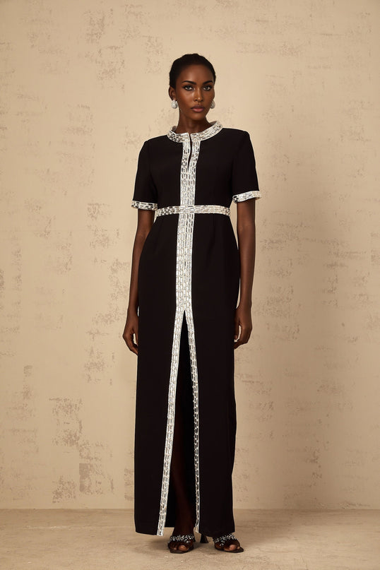 A black maxi dress with a front slit and crystal embellishments worn by a model standing against a plain background