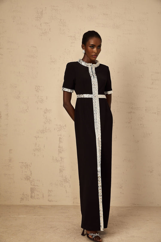 A black maxi dress with a front slit and crystal embellishments worn by a model standing against a plain background
