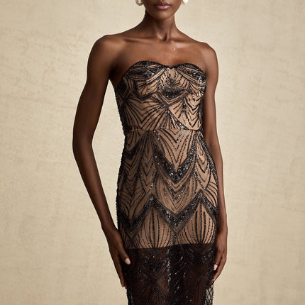 A black maxi dress with a sequinned corset bodice and sheer mesh skirt worn by a model standing against a plain background