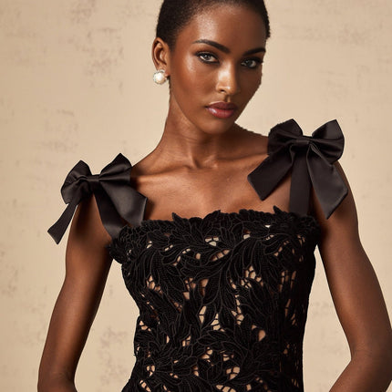 A black maxi dress with floral embroidery details worn by a model standing against a plain background