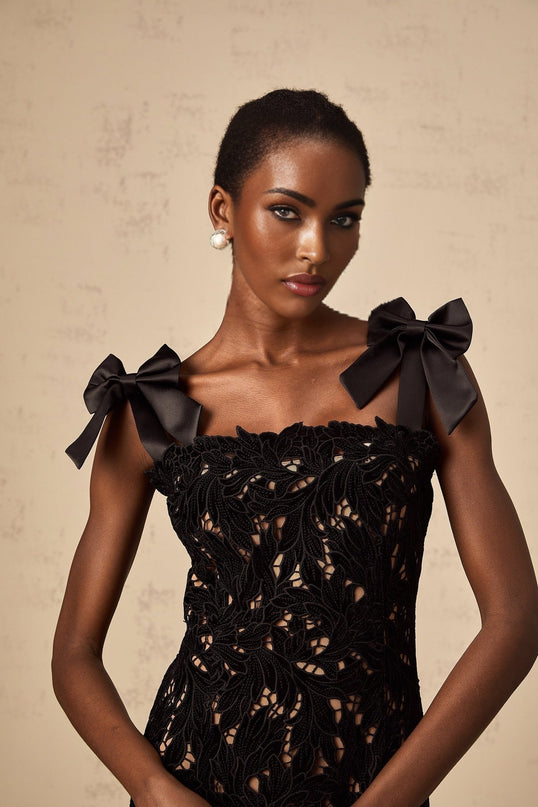 A black maxi dress with floral embroidery details worn by a model standing against a plain background